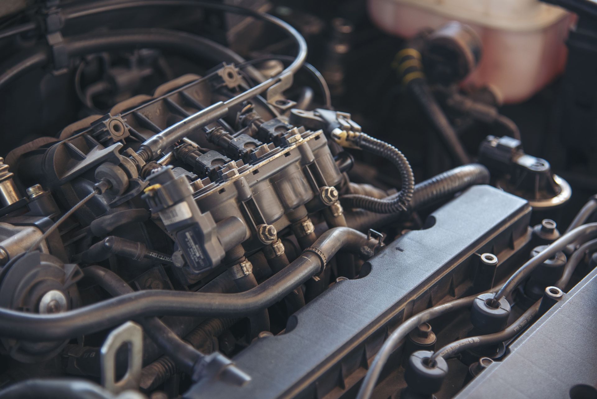 Visão aproximada do motor de um carro com vários componentes pretos, mangueiras e peças mecânicas sob o capô.