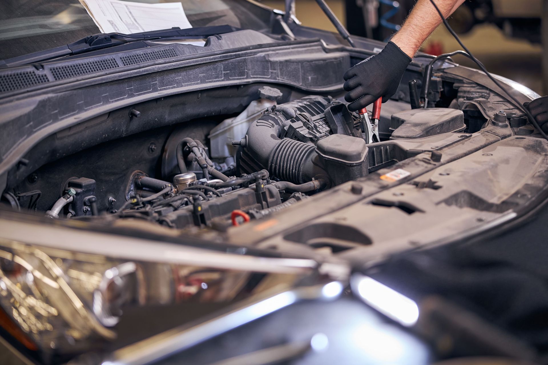 Um mecânico de luvas pretas trabalha no motor de um carro dentro de uma garagem.