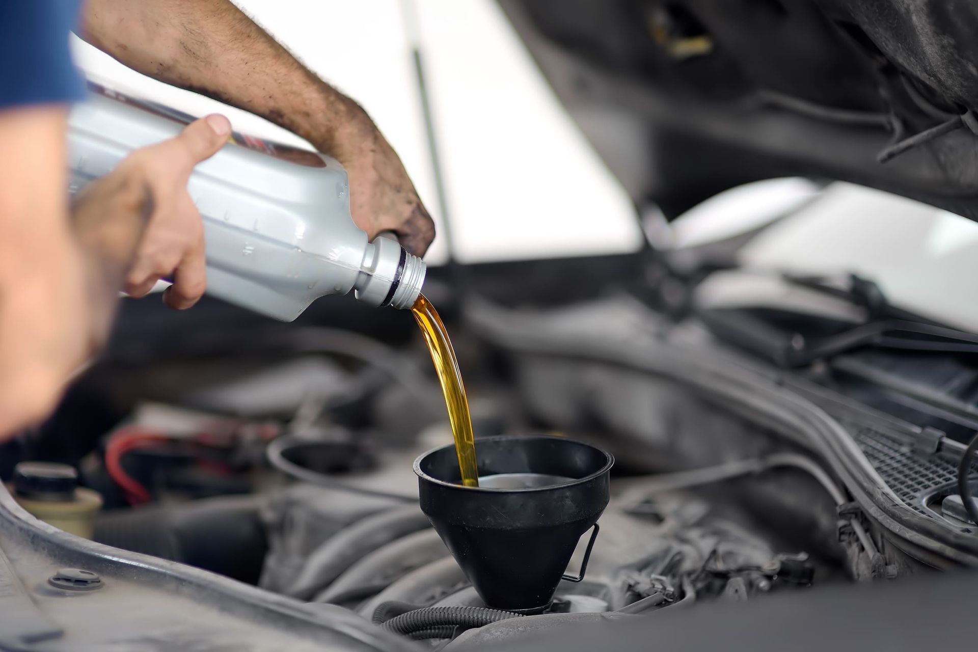 Pessoa despejando óleo de motor dourado de uma garrafa no motor de um carro usando um funil preto.