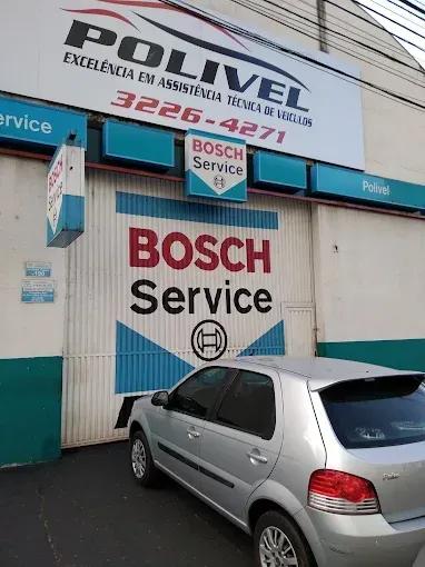 Carro prateado estacionado em frente a oficina mecânica Polivel Bosch Service, com uma placa e um telefone bem visíveis.
