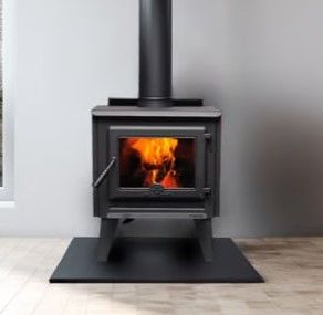 A wood stove is sitting in a room next to a window.