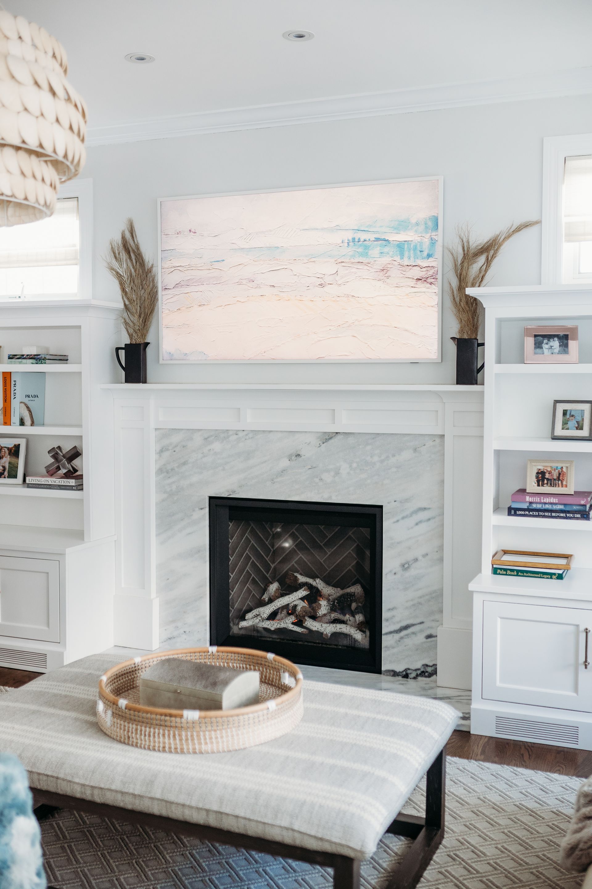 Living room with white fireplace, artwork, bookshelves, and striped ottoman.