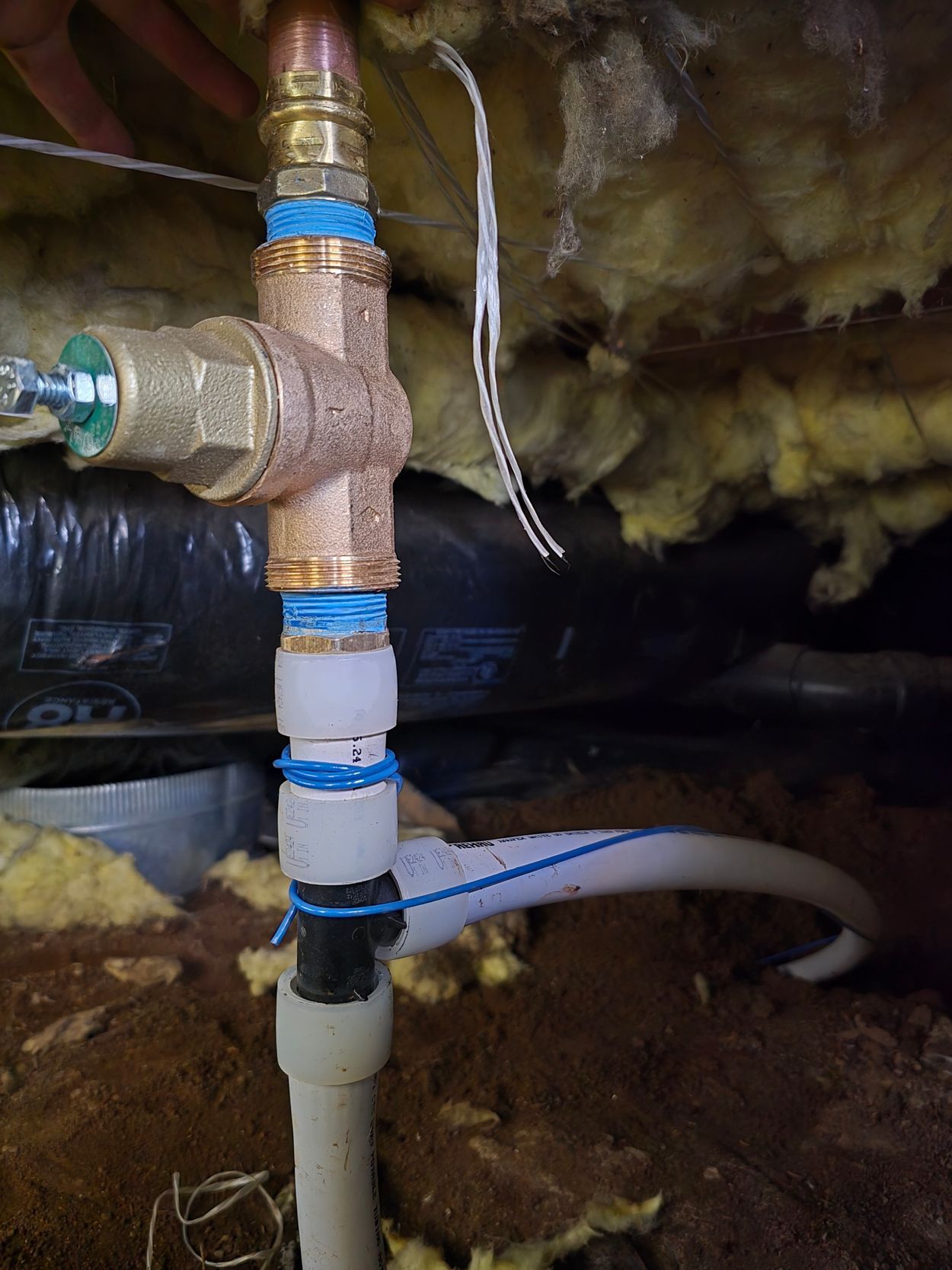 Close-up of insulated plumbing pipes and brass valve under a sink or floor, with a blue hose attached.