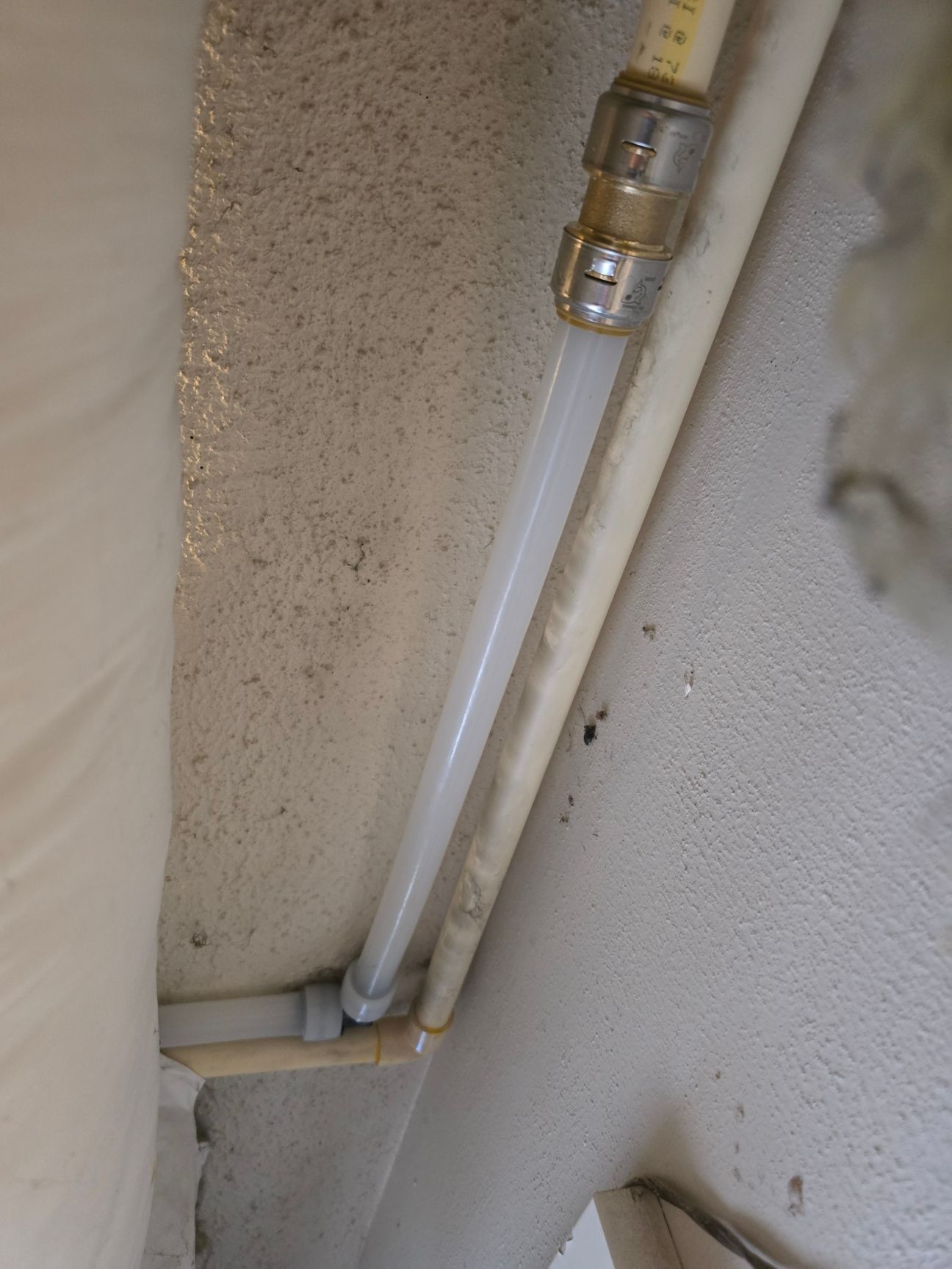 White pipes with metal fittings running along a beige wall in a narrow corner.