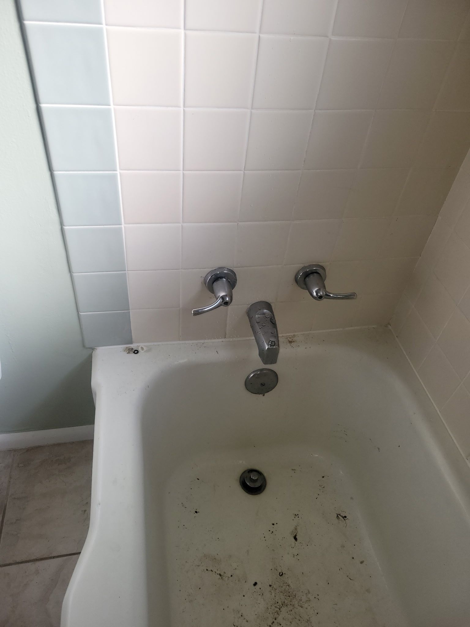 Dirty bathtub with tiled wall, faucet, and drain, showing grime and stains.