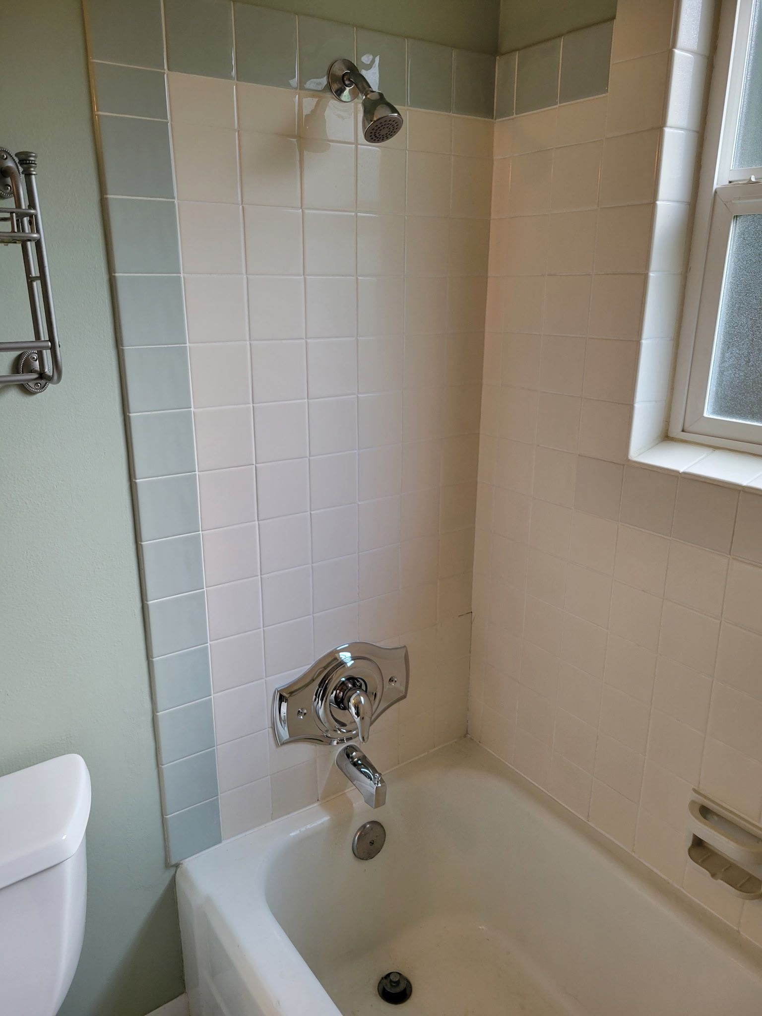 Small bathroom shower and tub with white tile, chrome fixtures, and a window.