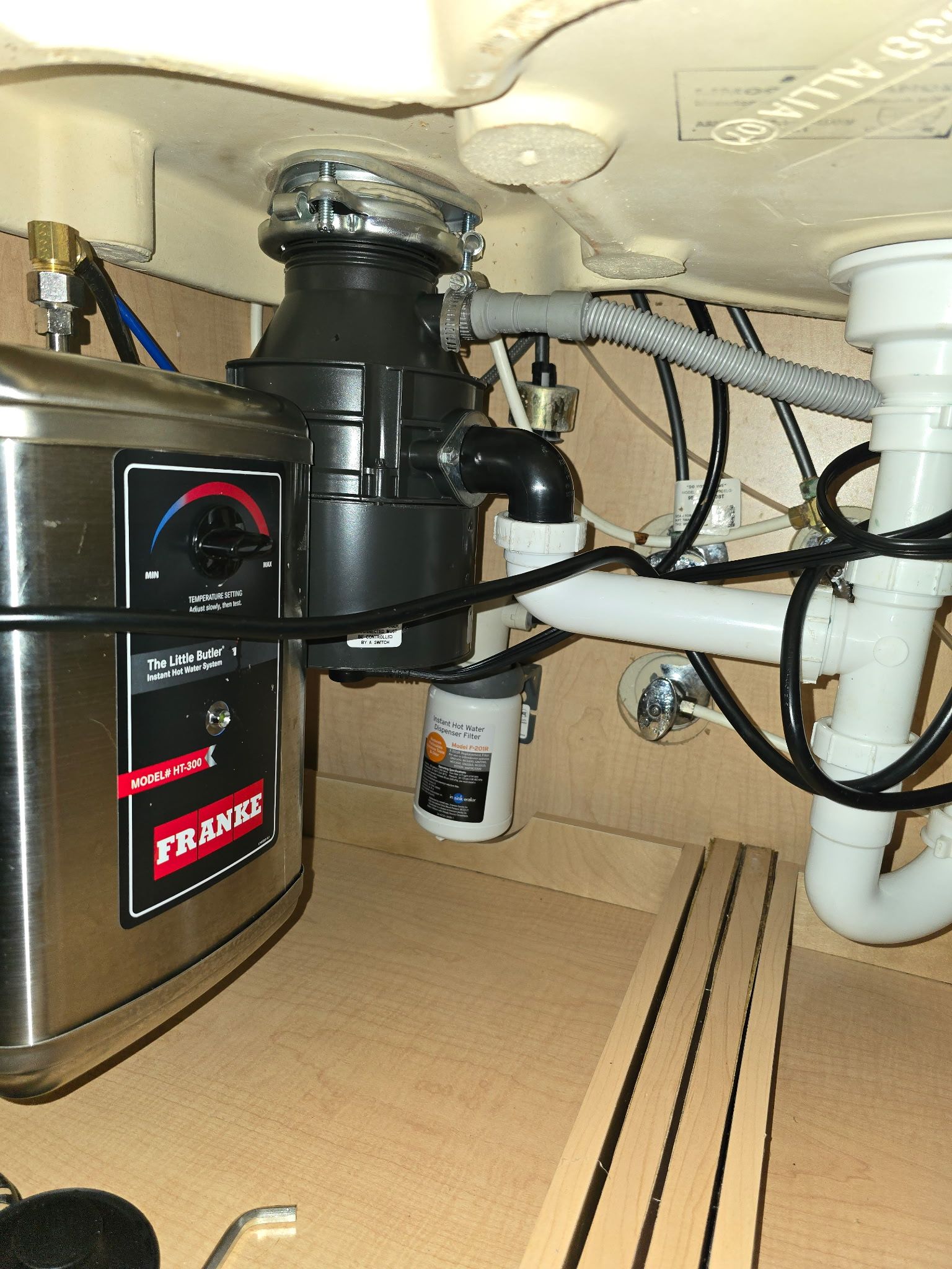 Under-sink view of a kitchen garbage disposal and plumbing pipes in a cabinet