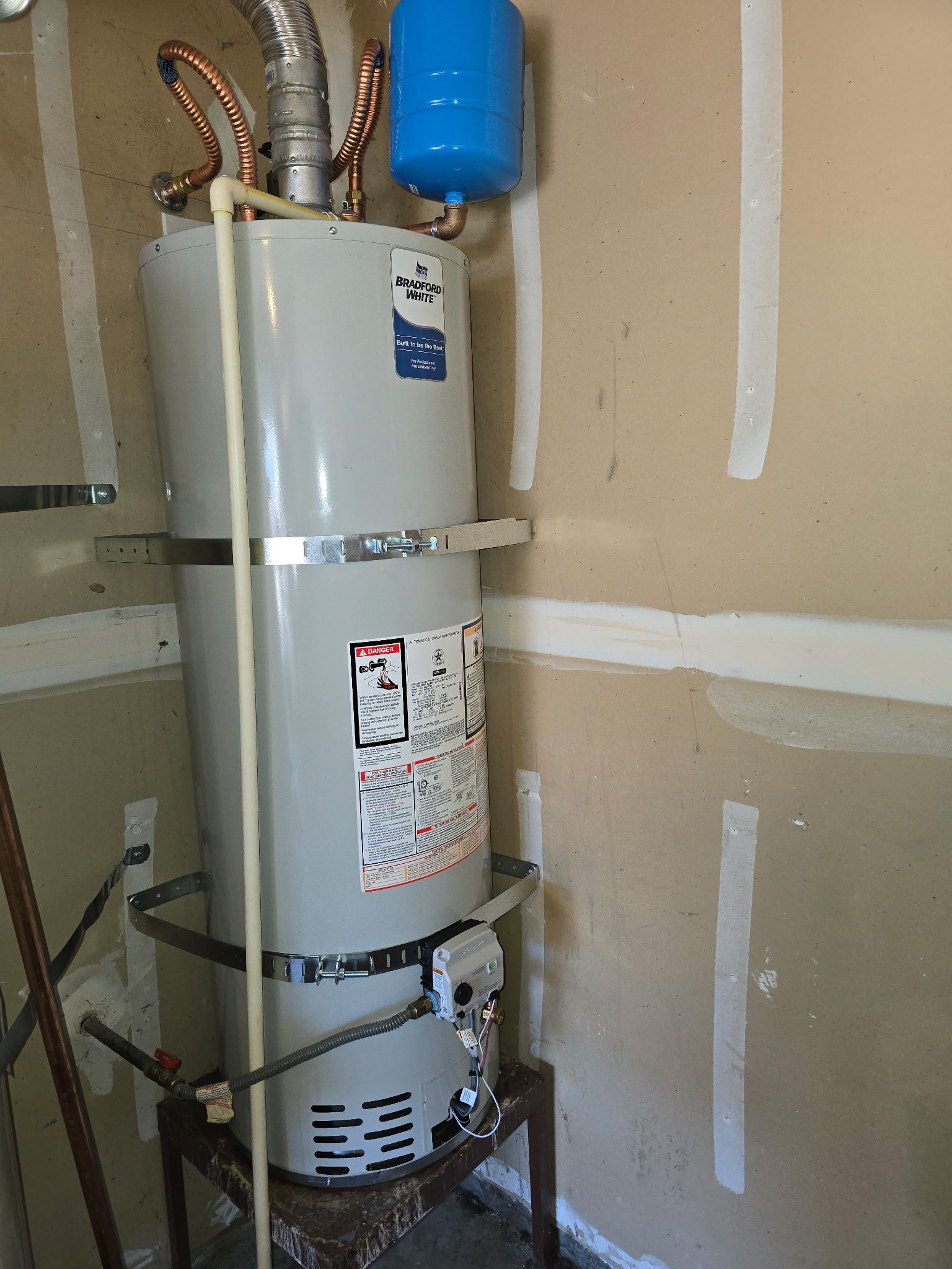 White water heater tank with copper pipes in an unfinished garage or utility room.