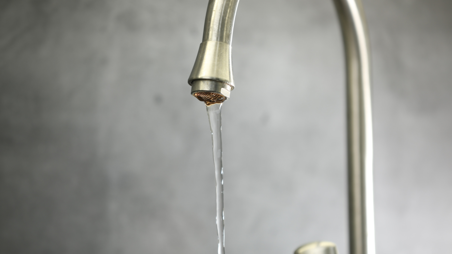 Water dripping from a chrome faucet into a sink against a gray background