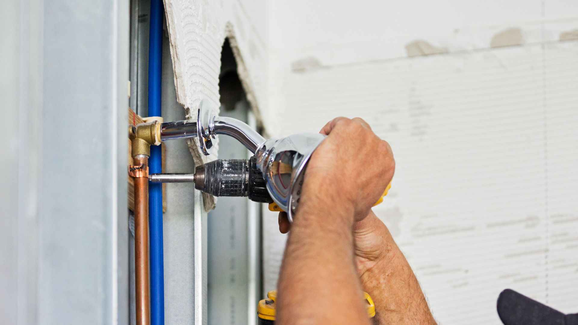 Person using a power drill to install a fixture on a wall near exposed pipes