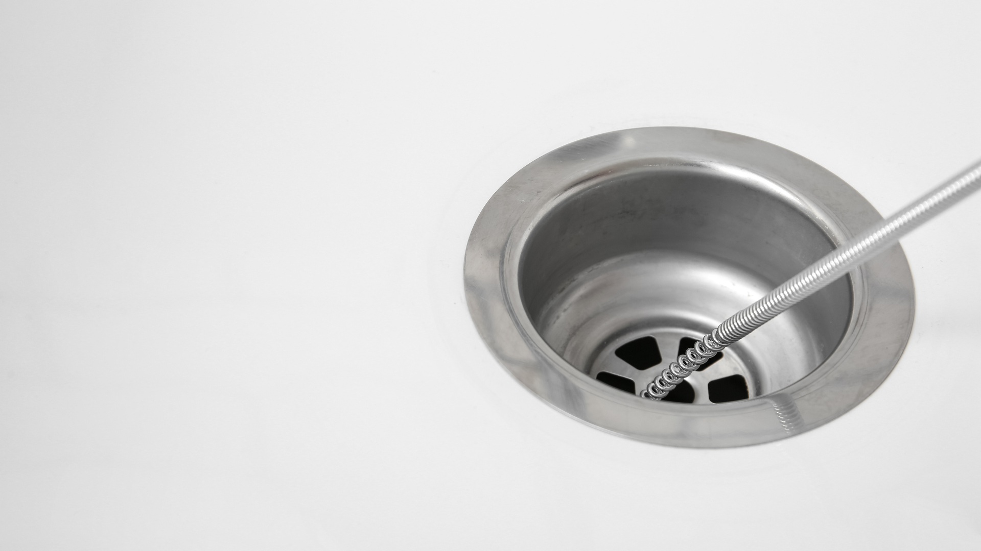 Stainless steel kitchen sink drain with a metal utensil inserted into the drain opening