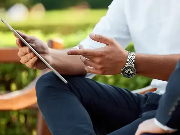 Two men are sitting on a bench looking at a tablet.