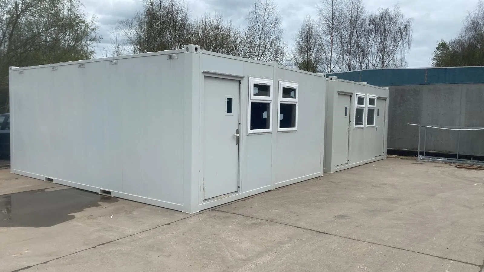 Two connected portable office buildings with doors and windows, set on a construction site.