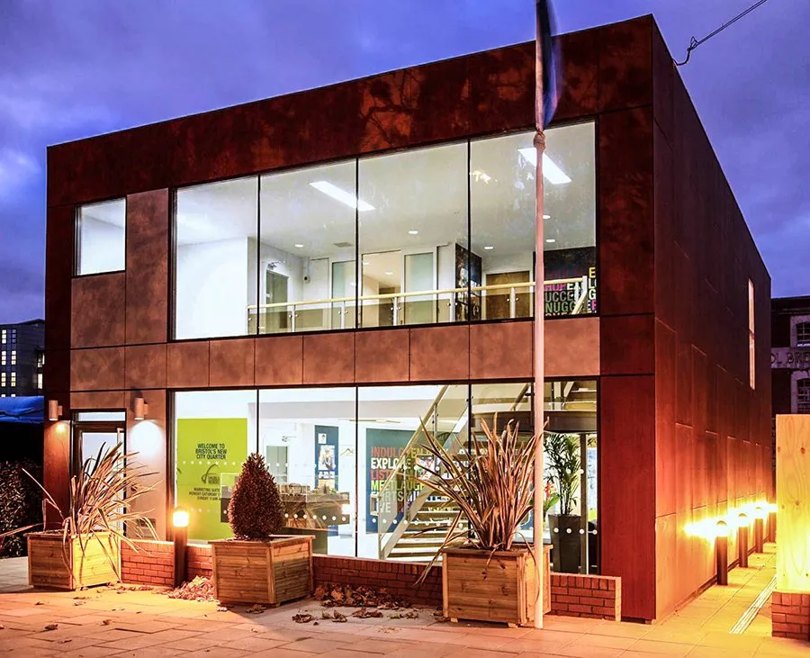 Modern office building with large glass windows and night-time lighting.