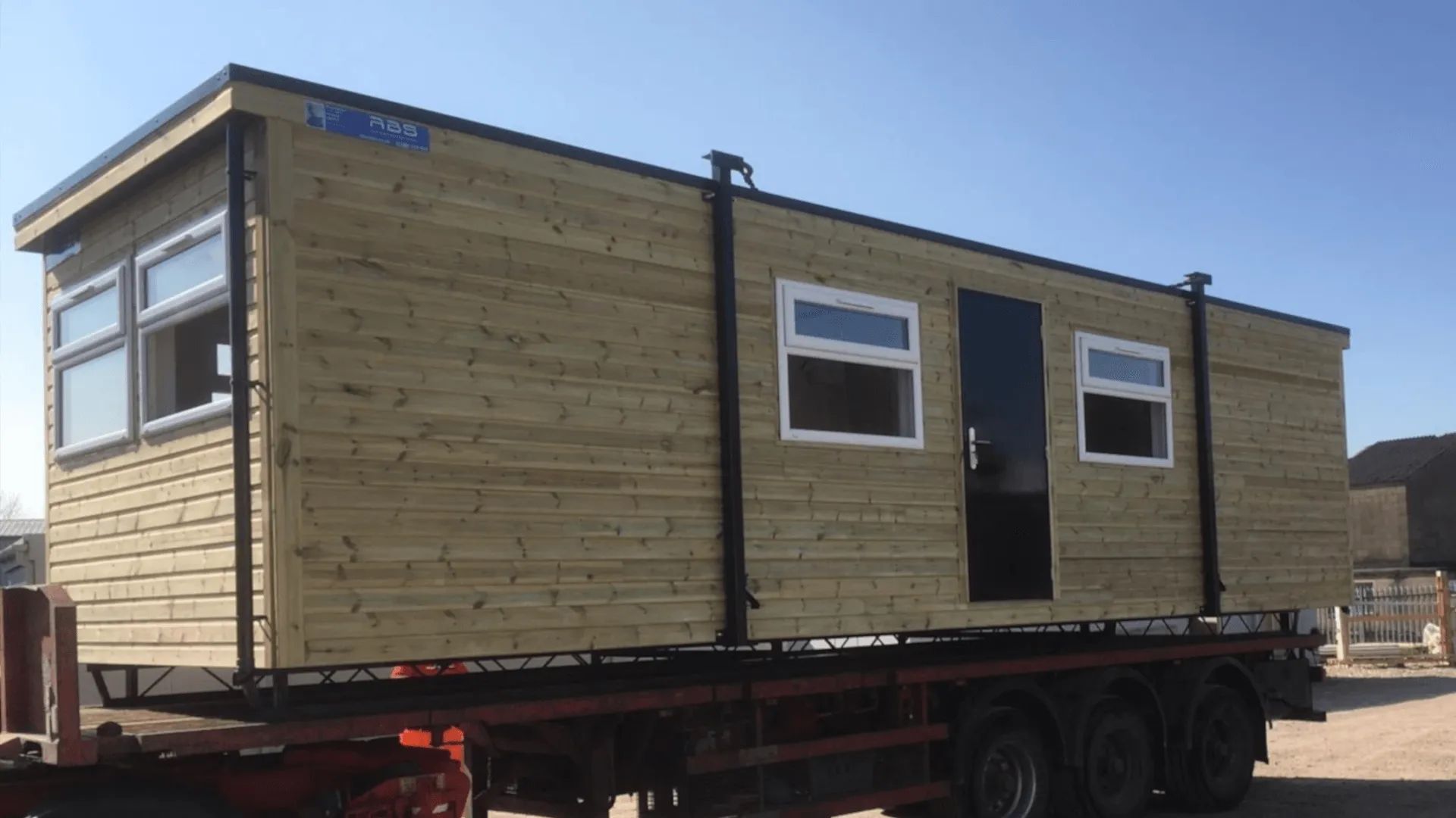 Wooden portakabin with a slight roof overhang, positioned on the back of a trailer