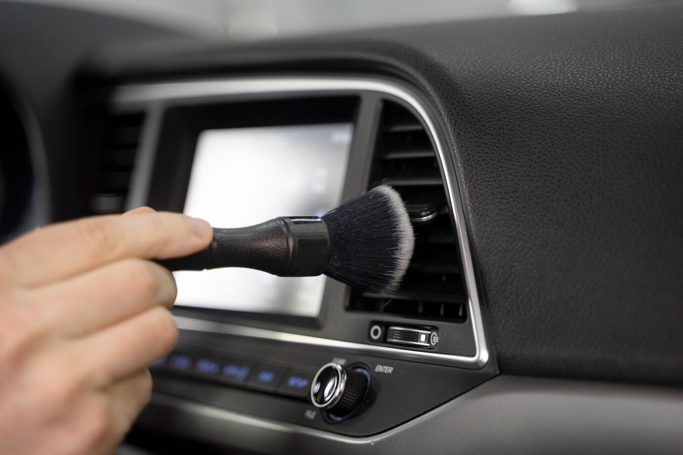 A person is cleaning the air vent of a car with a brush.