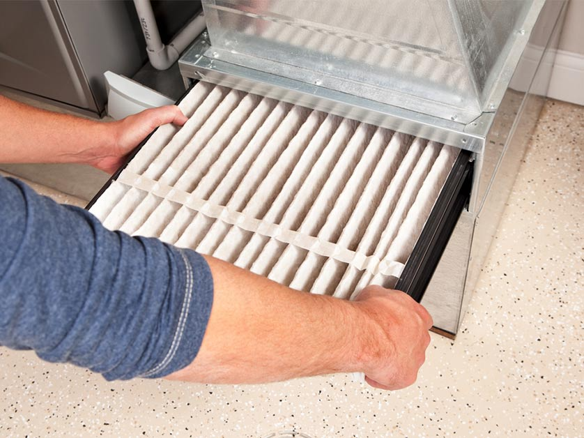 Person removing a rectangular air filter from a metal housing, indoors.