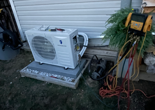 An air conditioning unit on a gravel-filled base, being serviced by equipment with colored hoses.