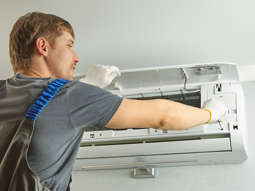 Technician in work gloves servicing an AC unit. He is opening the unit panel.
