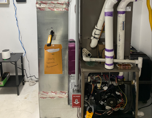 Furnace and ductwork in a utility room; a manila envelope with writing taped to the ductwork.