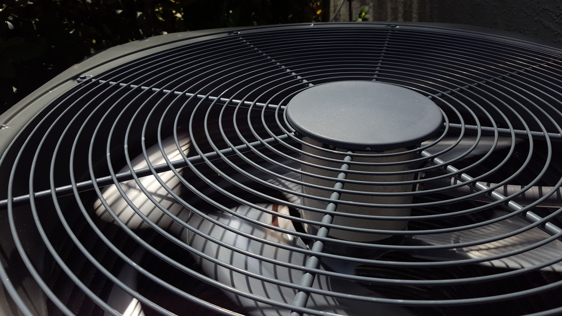 A close-up view looking down into the black metal protective grill and internal fan of an outdoor air conditioning unit.