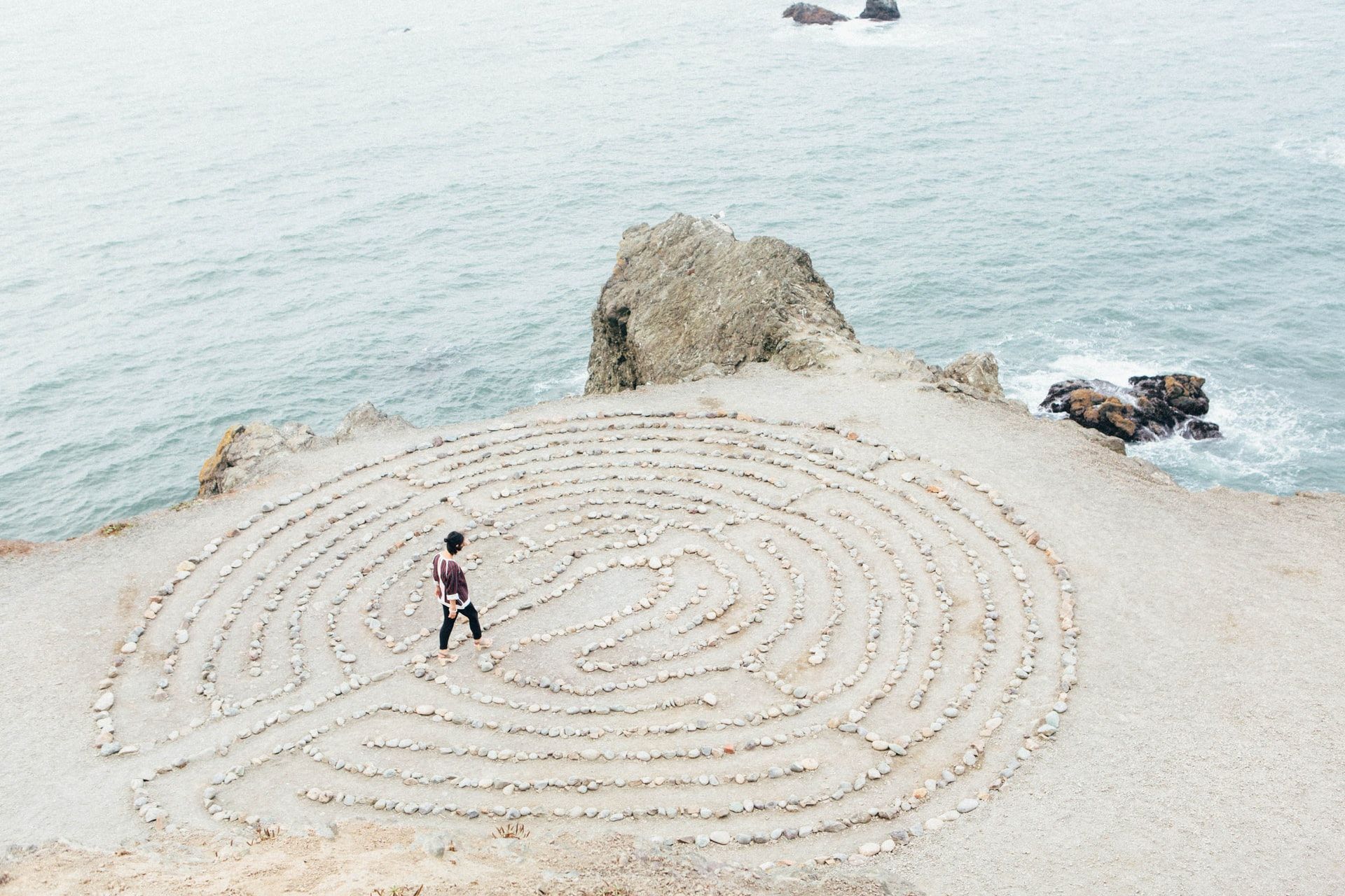 Stonemandal with labyrinth on a coast beach with person walking along