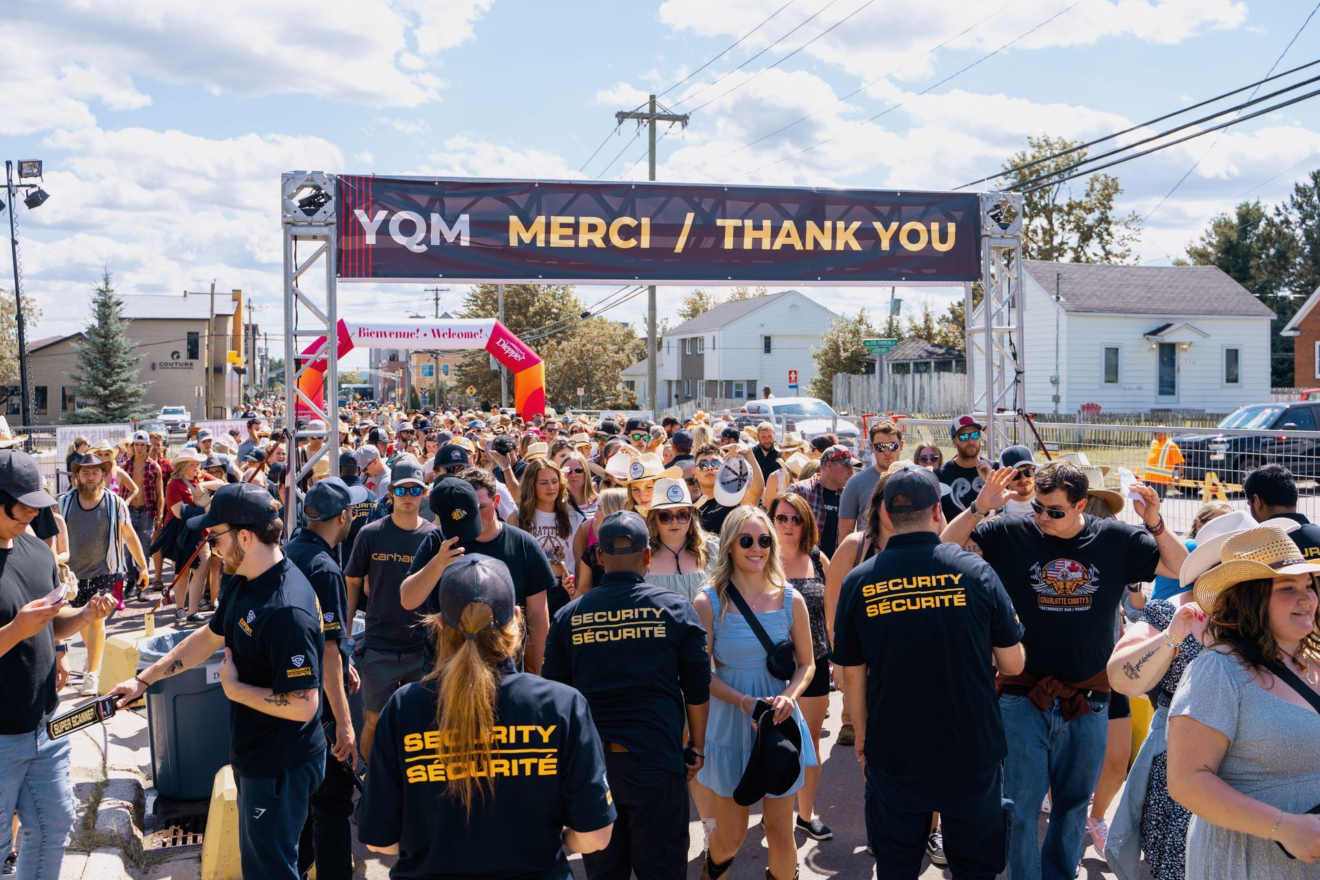 A large crowd of people are gathered under a sign that says merci / thank you.