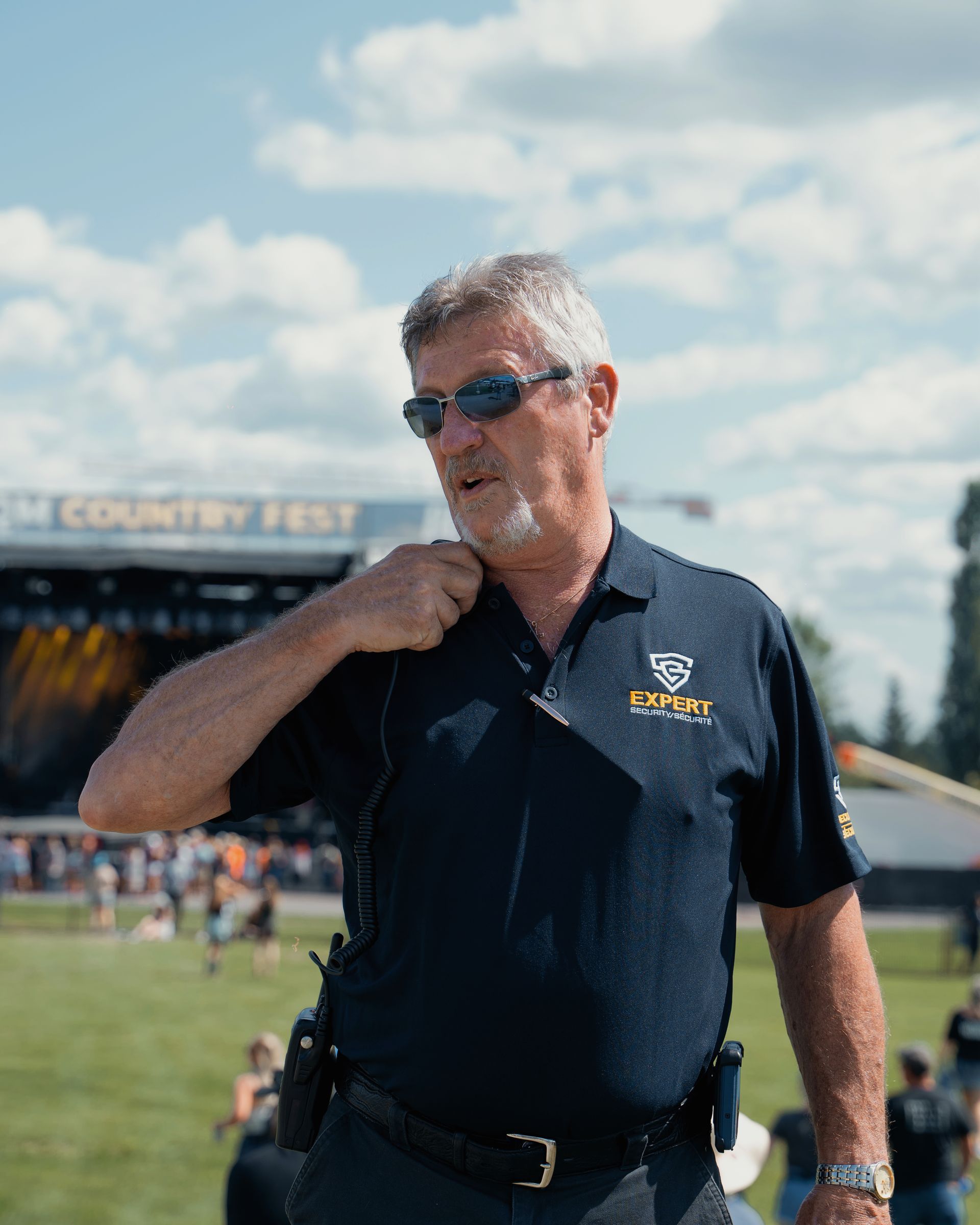 A man wearing sunglasses and a black shirt is standing in a field.