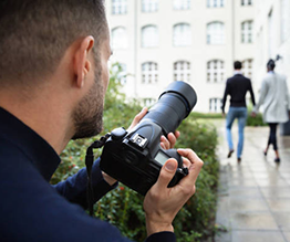 A man is taking a picture of a couple walking down a sidewalk with a camera.