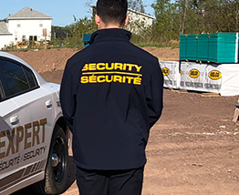 A man wearing a security jacket stands in front of a car