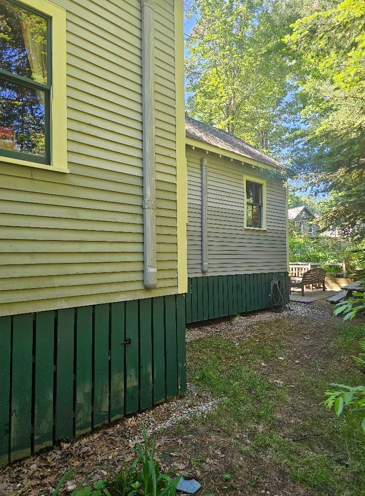 Green and yellow clapboard buildings with dark green foundations; path and trees.