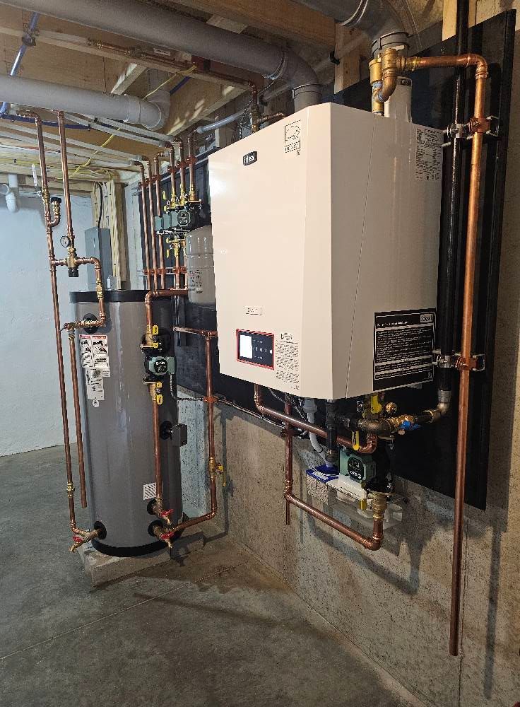 Plumbing system in a basement.  Copper pipes connect a water heater and a white rectangular boiler on a black board.