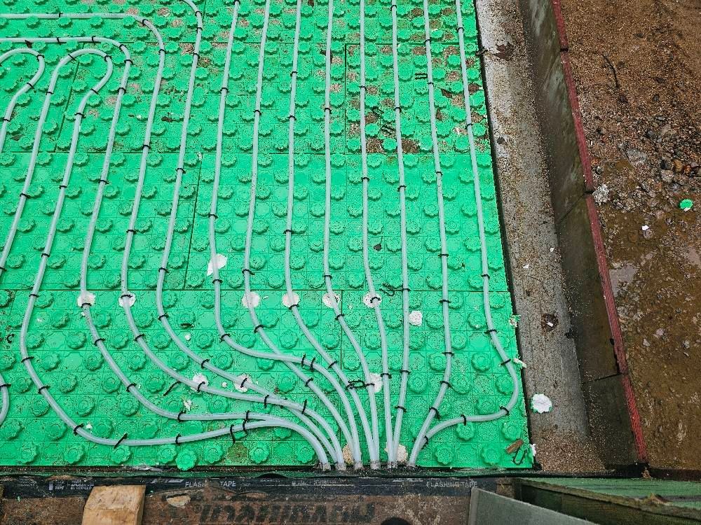 Green underfloor heating system installed, with white tubing radiating from a central point.