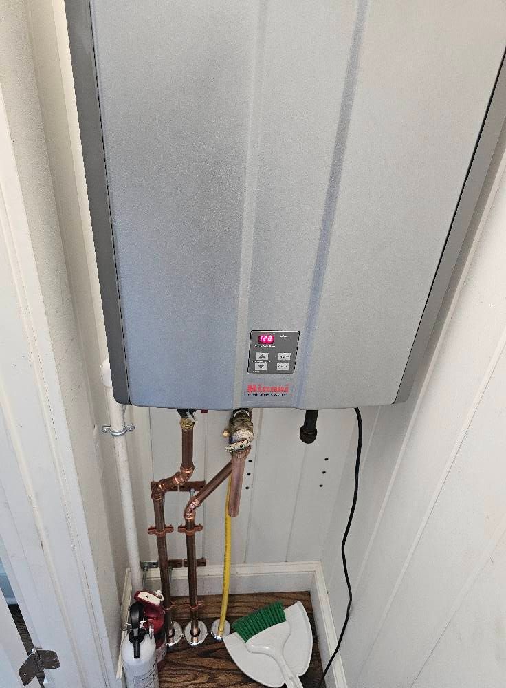 Gray tankless water heater on white wall with copper pipes.