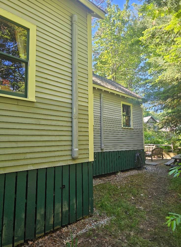 Two-toned green wooden buildings with dark green foundations, beside a pathway, with trees in the background.