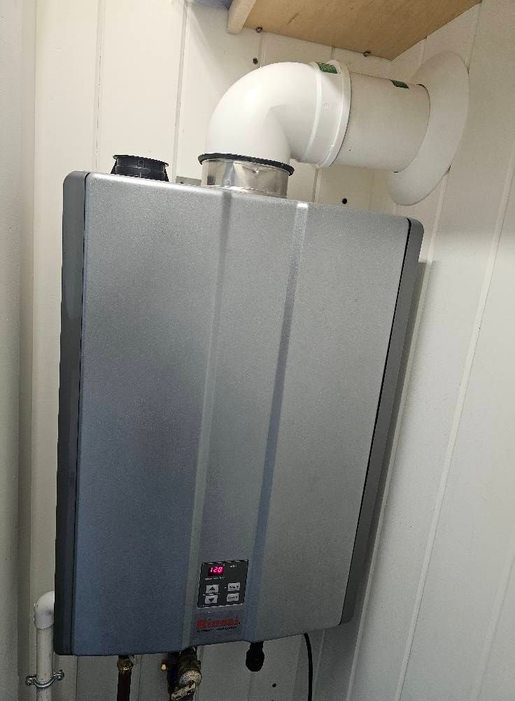 Gray and silver tankless water heater mounted on a white wall, venting through a white pipe.