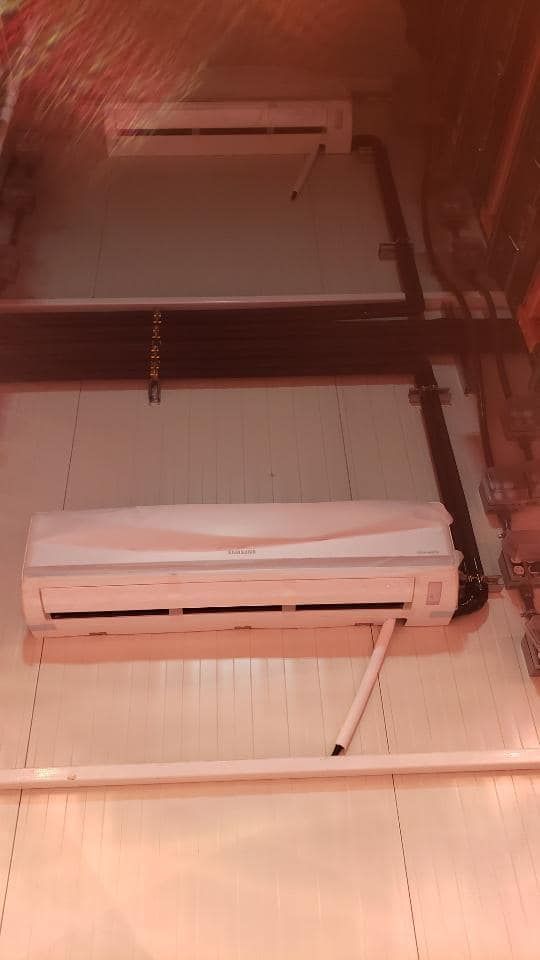 Two white air conditioning units mounted on a wall, with black pipes.