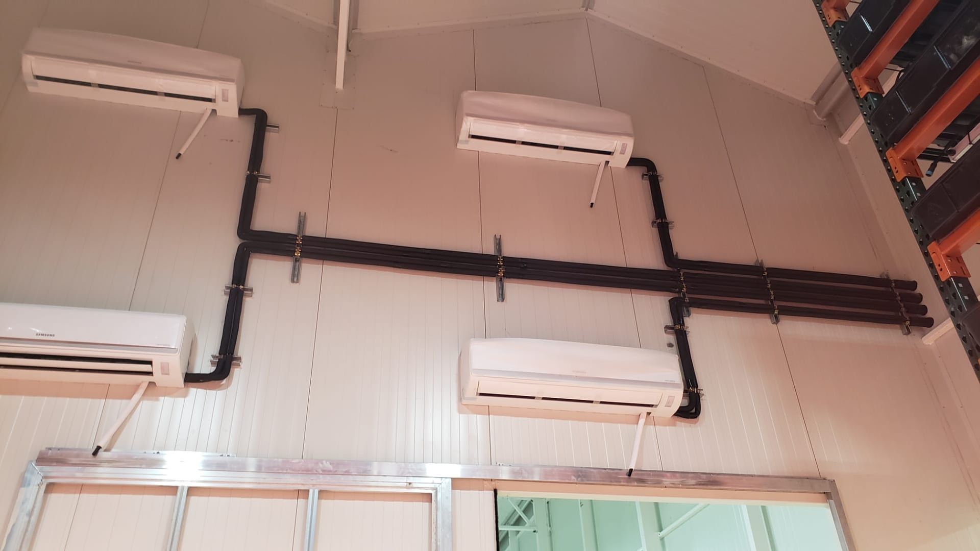 Four wall-mounted air conditioning units with black piping on a white wall.