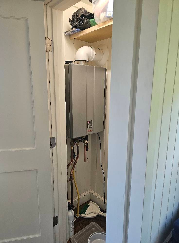 A tankless water heater installed inside a narrow closet. White door frame surrounds the unit.