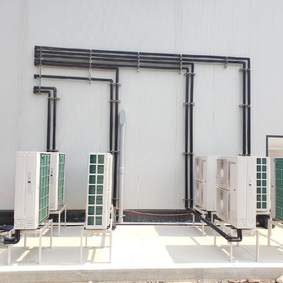 Air conditioning units installed outside a building; black pipes connect the units to each other.