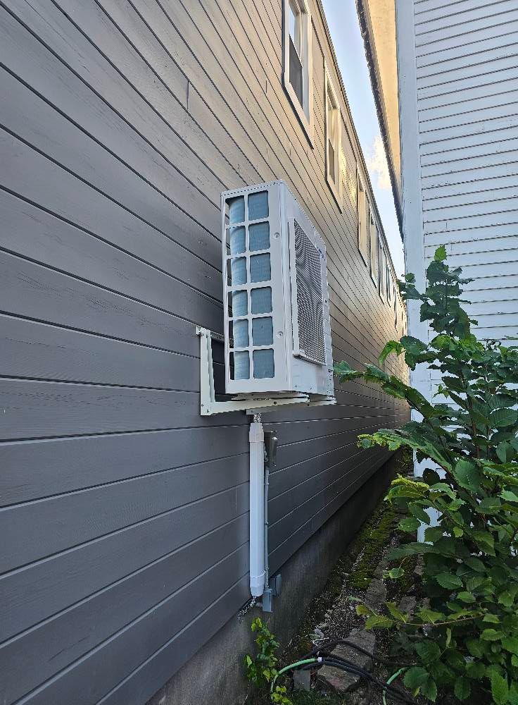 Air conditioner mounted on the side of a gray building. White support bracket.
