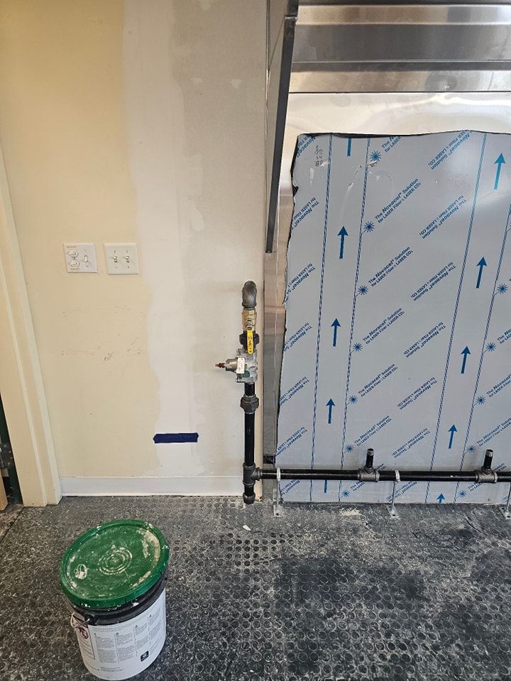 A commercial kitchen area under construction with gas pipes, a hood, and a paint bucket.
