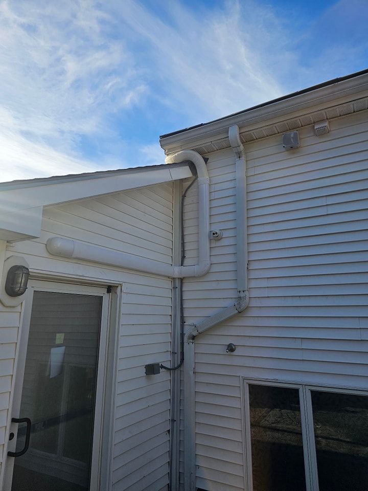 White house exterior with white pipes and wiring against a blue sky with clouds.