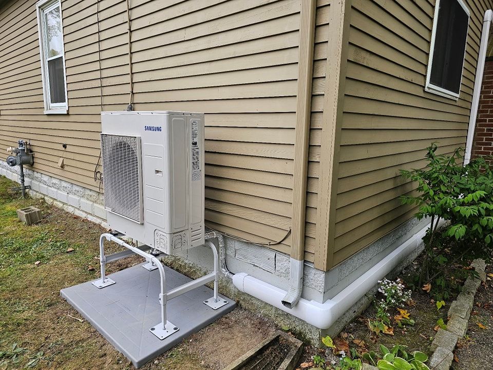 Air conditioning unit on a concrete pad outside a tan-sided house with white trim.