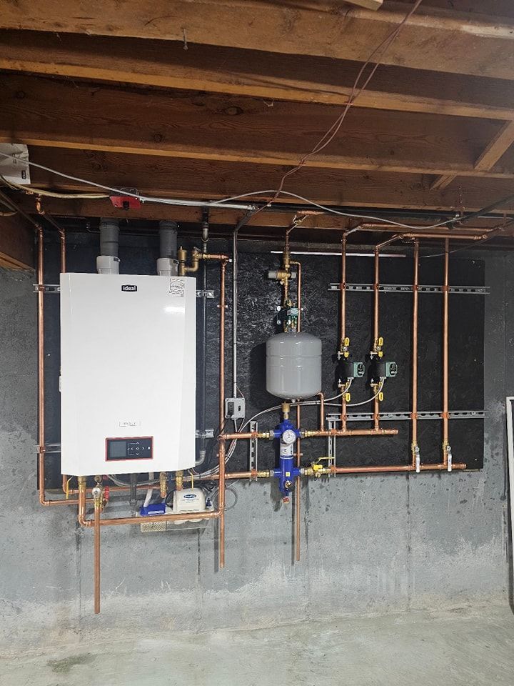 White wall-mounted boiler with copper pipes, connected to other components, installed on a basement wall.