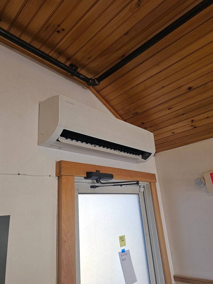White air conditioning unit mounted above a door. Wooden ceiling and trim surround.