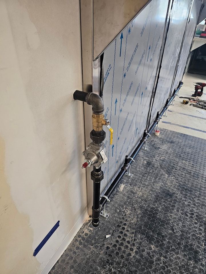 Gas pipe assembly mounted on a wall with a yellow valve and pressure regulator, in an industrial setting.
