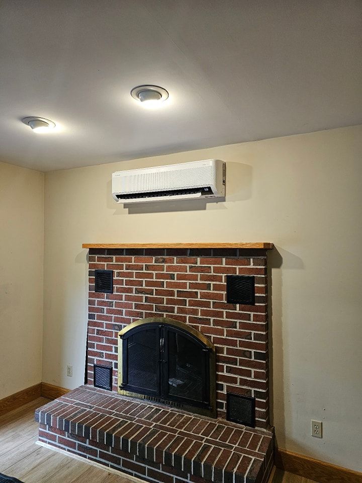 Air conditioning unit mounted above a brick fireplace in a room with light-colored walls.