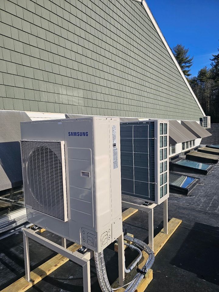 Air conditioning units on a rooftop with a green shingled building and blue sky in the background.