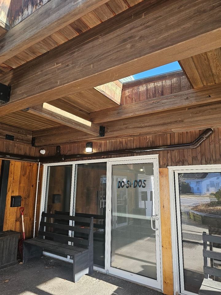 Exterior of a building with wooden beams, glass doors, and a bench. The address 
